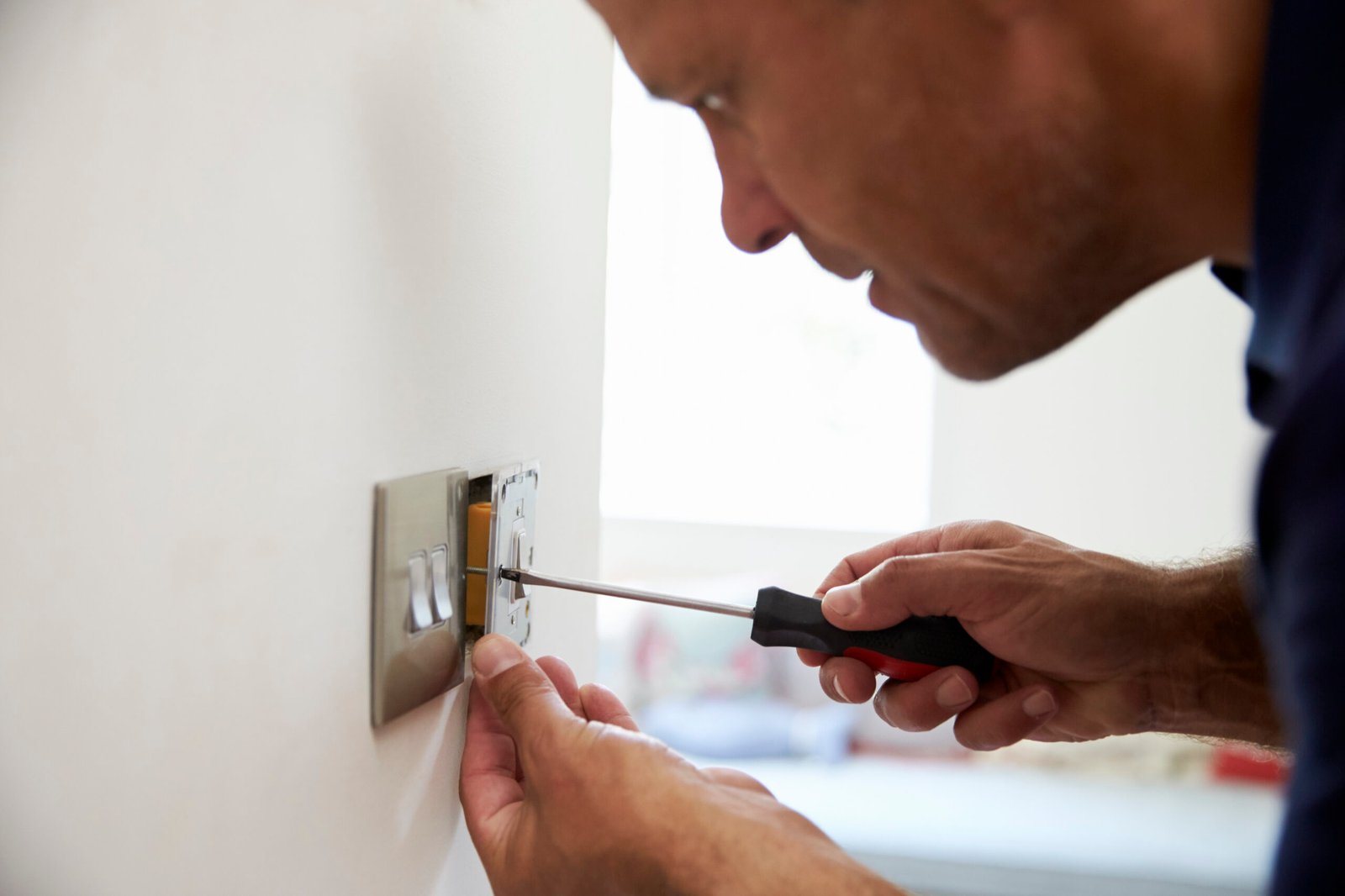 Mann schraubt einen Lichtschalter mit Schraubenzieher an der Wand fest